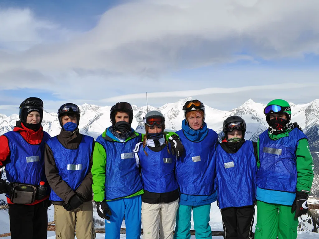Gruppe in blauen Leibchen posiert vor verschneiten Bergen.